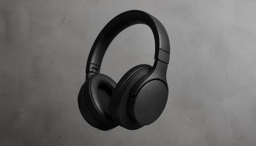 Minimalist studio product photography of a premium matte black wireless headphone, floating on a smooth concrete background. Soft, diffused studio lighting, subtle shadows, clean composition, elegant and modern aesthetic. Ultra-realistic, sharp focus on product texture, commercial grade. 8K.